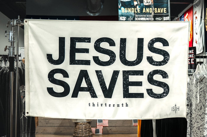 The 13th Jesus Saves Flag - Ivory hangs boldly in a clothing store, its striking black text standing out among racks of clothes and promotional signs for a powerful statement of faith.