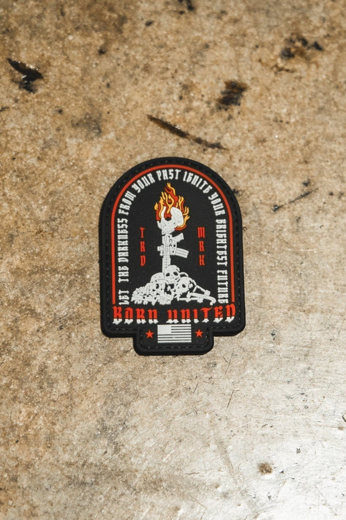 The Let The Darkness PVC Patch by Born United Private Label features a raised fist with a wrench, surrounded by text and “Work United” at the bottom in red, black, and white on a rugged brown surface.