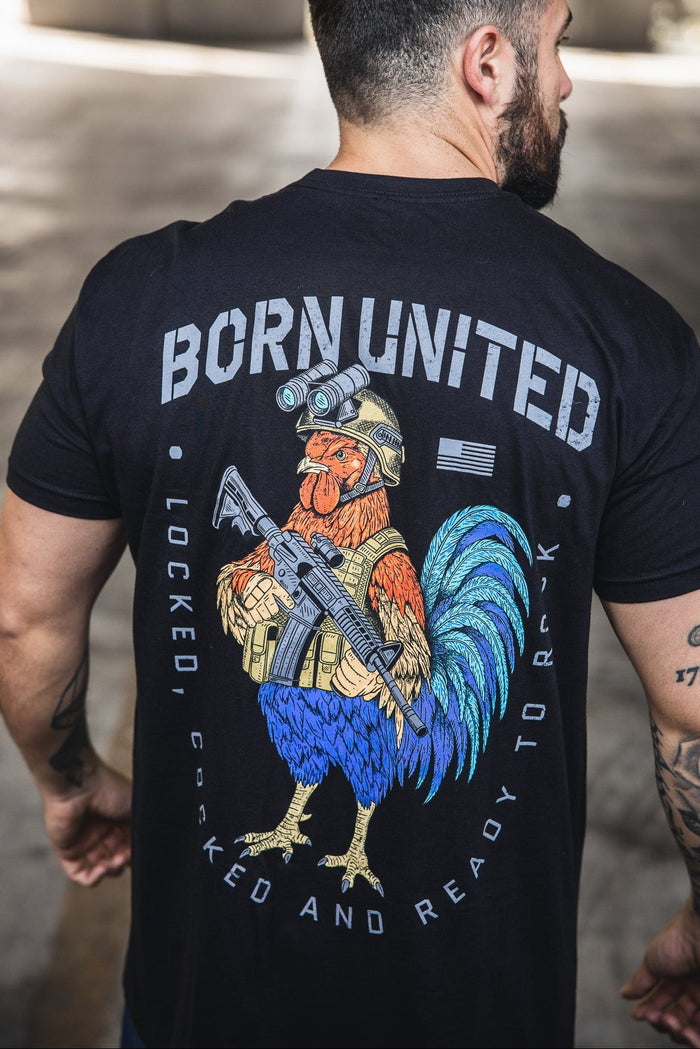 A man wears the "Battle Bird" black tee by Born United Private Label, a 60/40 blend featuring a rooster soldier with rifle and the phrases "BORN UNITED" and "LOCKED, COCKED AND READY TO ROCK" above and below the graphic.