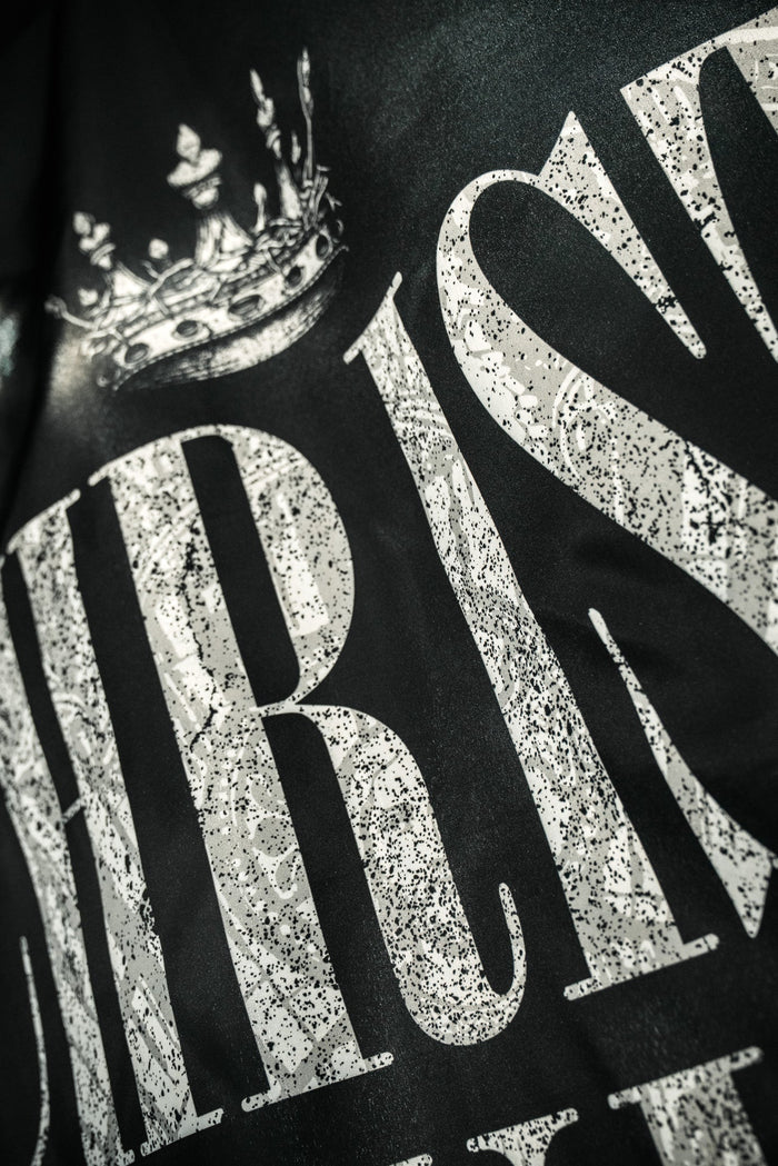Close-up of "CHRIST" in large, white, glittery letters with a crown above on a dark background. A striking design by 13th, perfect for displaying your faith with the Christ is King Flag.