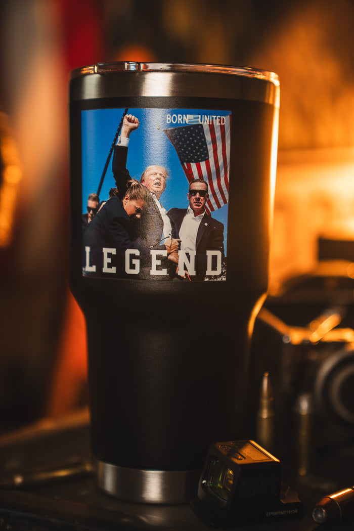 The Forever Legend Tumbler - 30oz by Born United Private Label features a photo of a man raising his fist by an American flag, with "LEGEND" printed below, set against a black background with others in the scene.