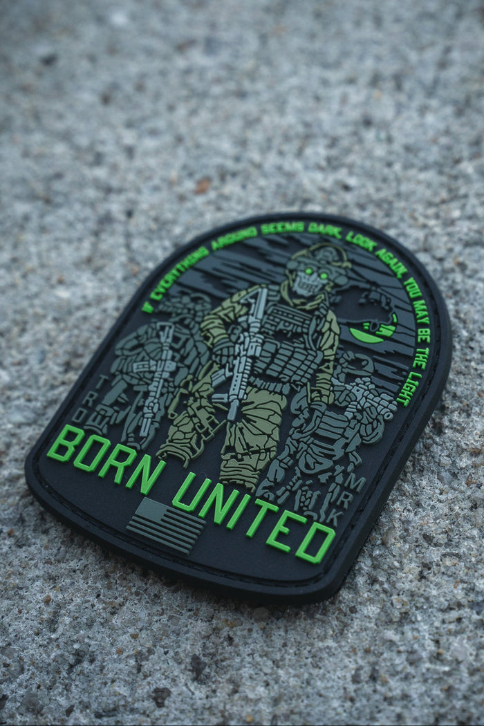 The Light in the Darkness PVC Patch by Born United Private Label features an armed soldier in night vision gear on concrete, "Born United" in bold green, and the quote: “Even if the world seems dark, look for the light. We are the light.”.