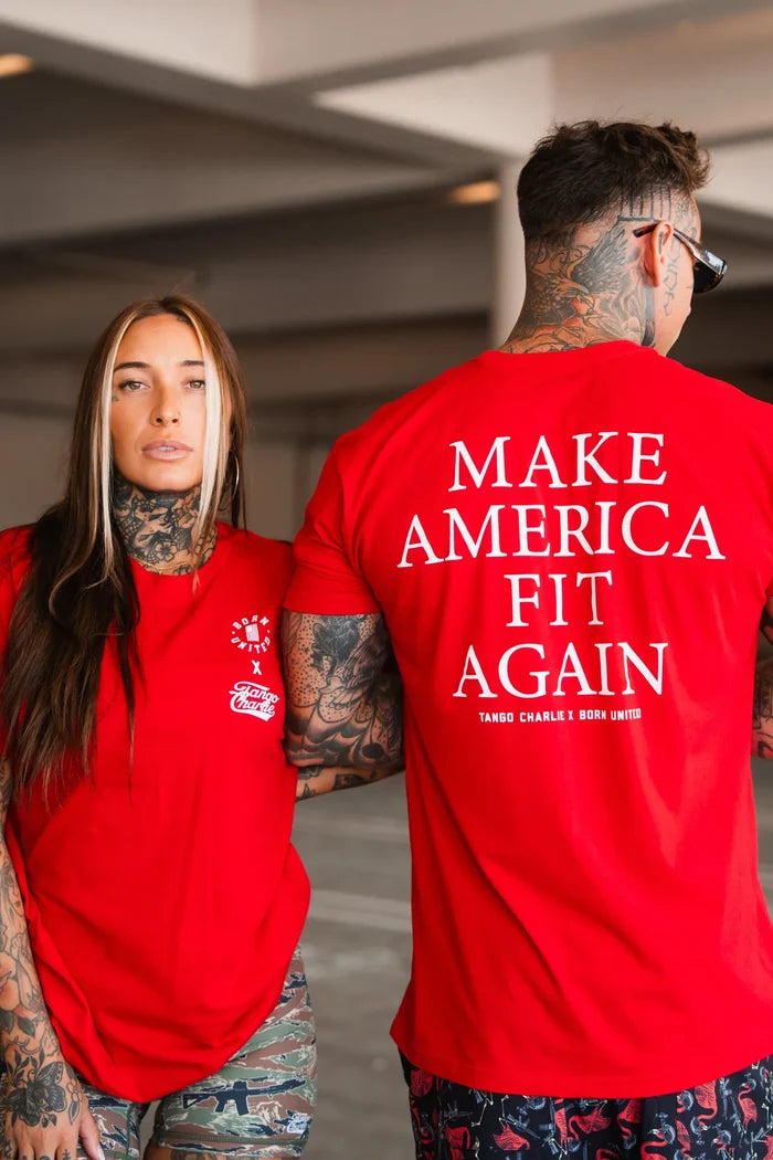 A woman faces forward and a man shows his back, both in red Tango Charlie Apparel tees; his shirt displays "Make America Fit Again"—the signature message of the Make America Fit Again - Tee.