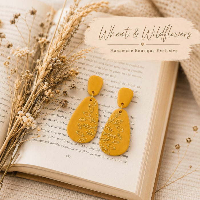 Tea-Shirt Shoppe mustard yellow teardrop dangle earrings with embossed botanical leaf patterns on an open book.